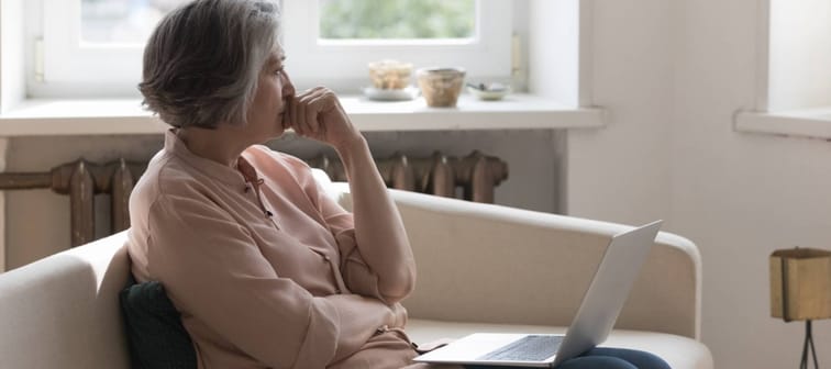 Woman looks off in distance with laptop on her lap/