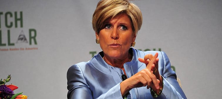 Suze Orman counts something on her fingers on stage.