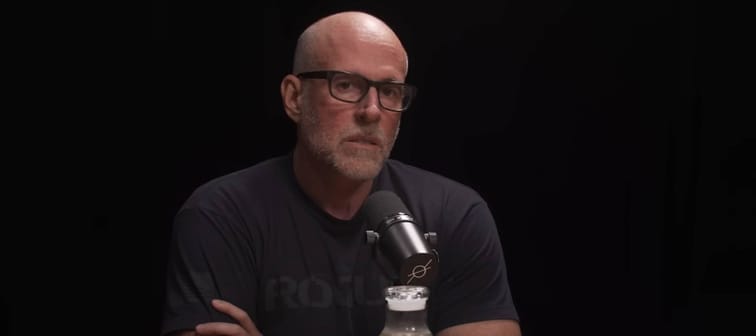 Scott Galloway sits in dark podcast studio with arms crossed, looking upset.