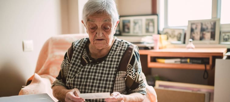 Senior woman looking at a piece of paper in her hand, sitting on a couch.