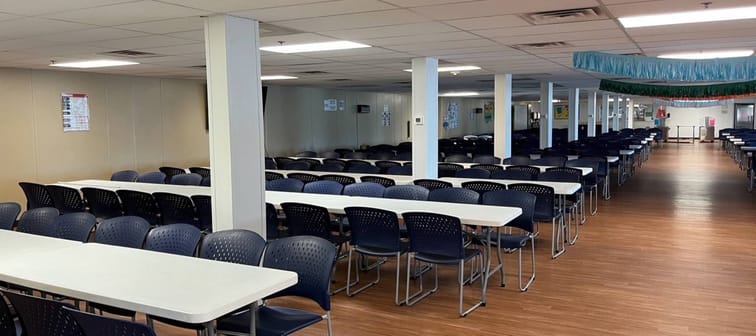 Empty room with rows of tables with empty chairs at them.