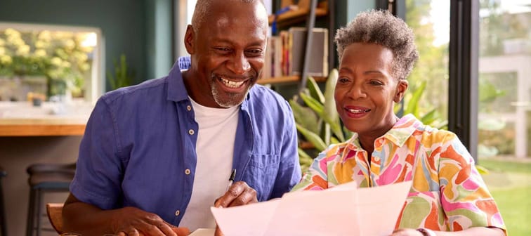 Smiling Senior Couple Sitting Around Table At Home Reviewing Finances