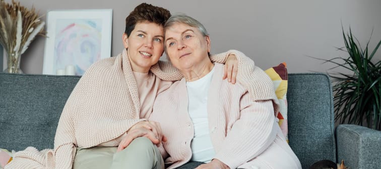 Senior woman sitting with adult child on a couch with a blanket