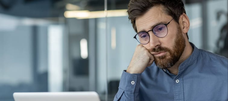 Close-up photo of a bored and tired young man in a blue shirt and glasses, resting his head.