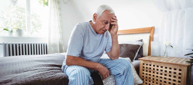 Frustrated senior man sitting on bed in bedroom