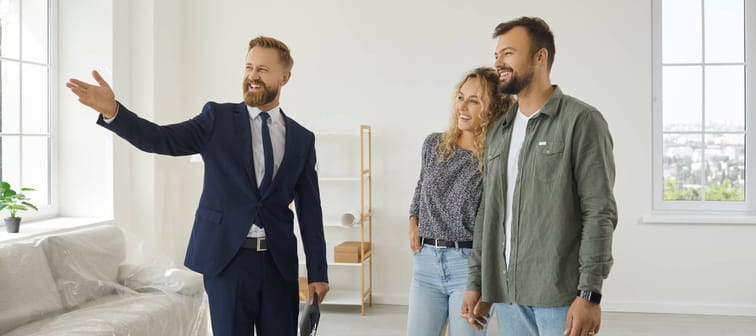 A real estate agent showing a clean, bright rental property to a pair of smiling 30-somethings.