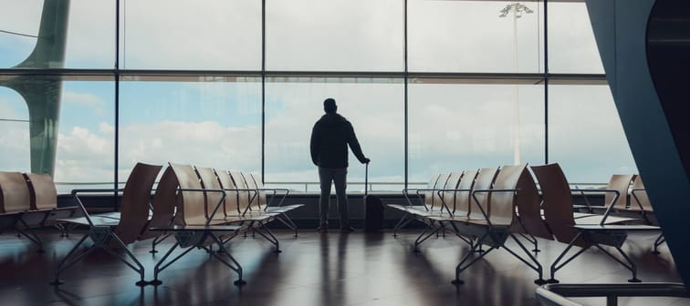 Man standing alone in an airport looking out glass windows