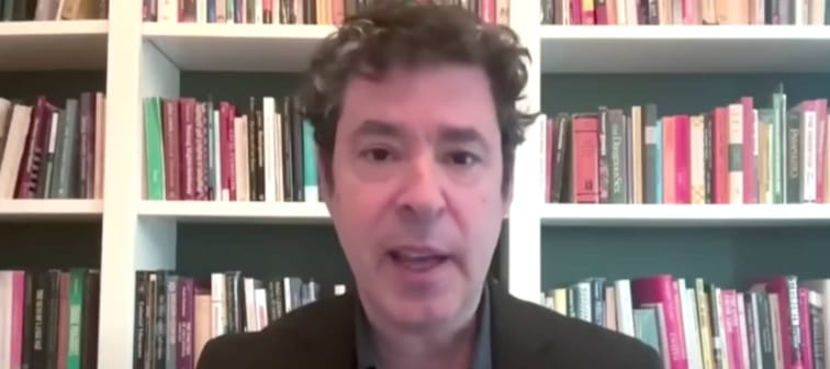 Man on camera in front of book shelves.