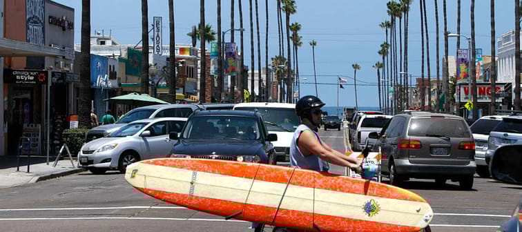 Man rides motorcycle while carrying surfboard.