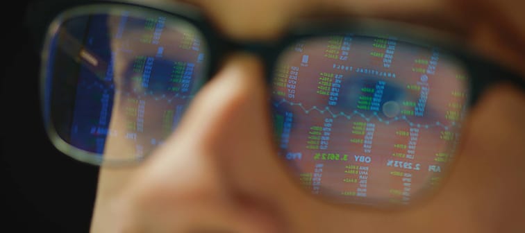 Man with stock market charts reflected in glasses.