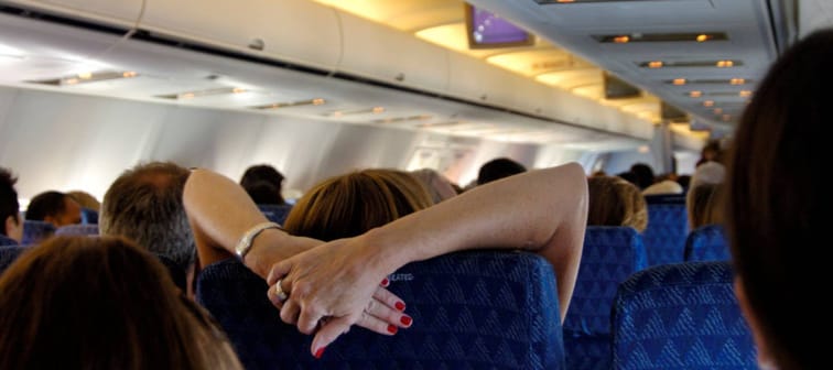 A woman folds her arms behind her headrest on a plane.