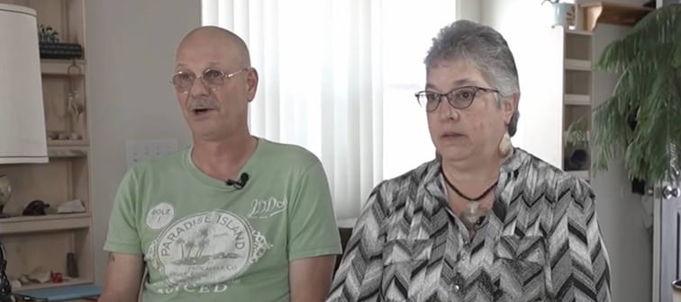 Couple seen in their living room, talking to camera, unhappy.