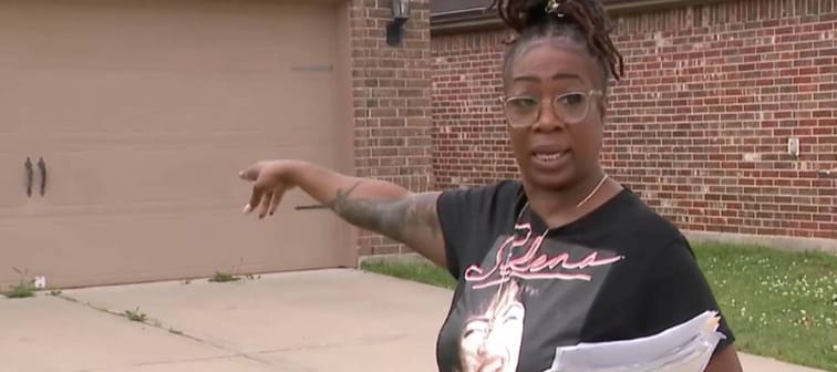 Woman holding papers pointing at house.