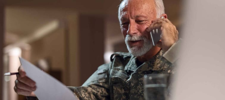 Happy mature veteran in army uniform communicating on cell phone while doing paperwork in the office.