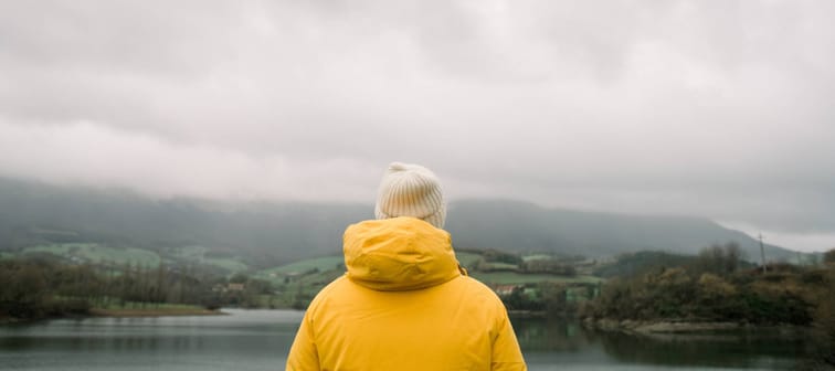 Person in yellow coat looking out at scenery at lake.