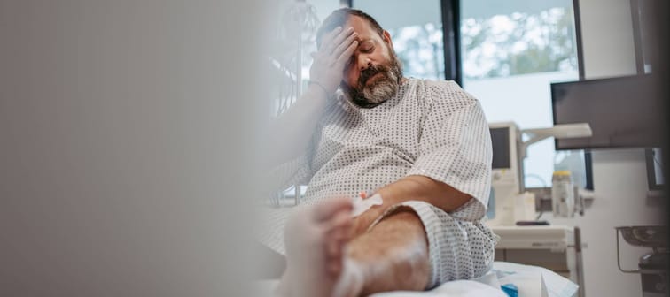 Middle aged man in hospital gown sitting on bed