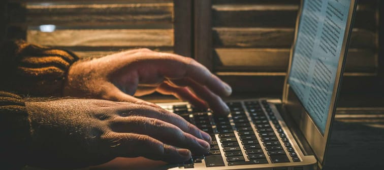 Man hands typing in MacBook Air Laptot beside wooden window