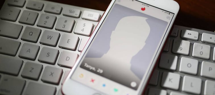 A smartphone with a male profile on screen lays on a keyboard.