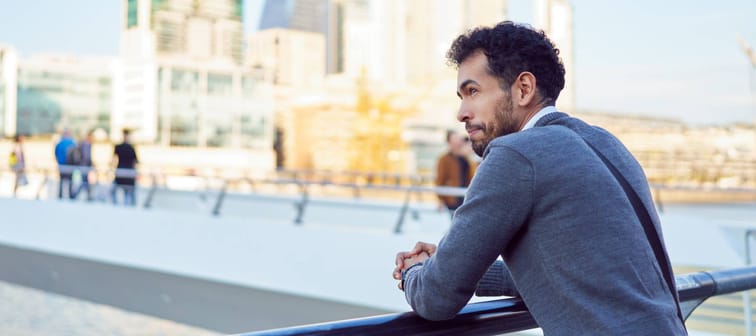 Young man leans on railing outside in city