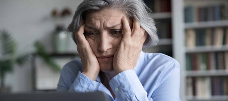 Frustrated senior retired woman touching head, looking at laptop screen with despair, getting bad news, reading online chat message, email letter. Problem with computer concept