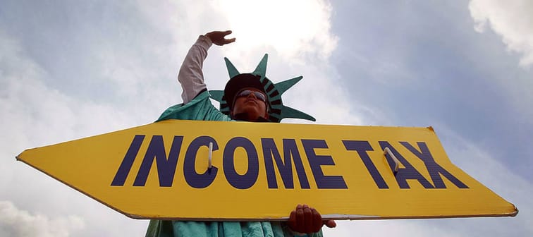 Man wearing Lady Liberty costume, holding 'Income Tax' sign.
