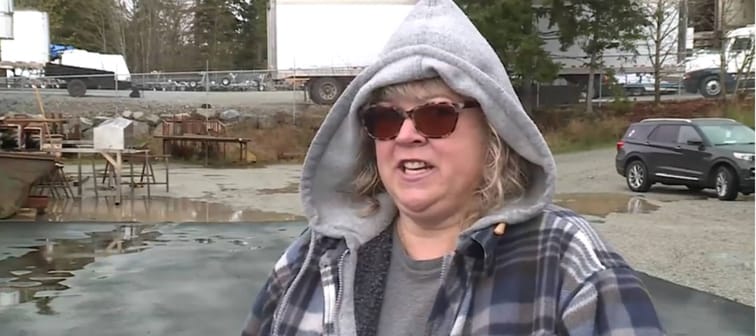 Woman being interviewed in parking lot, wearing grey hoodie and sunglasses.