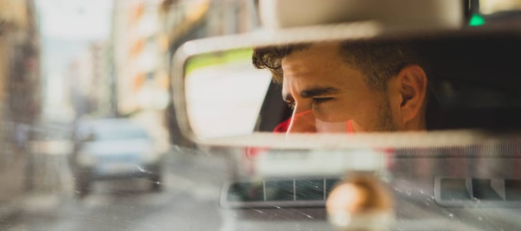 Man seen in the reflection of the rearview mirror, looking unhappy and out at traffic.