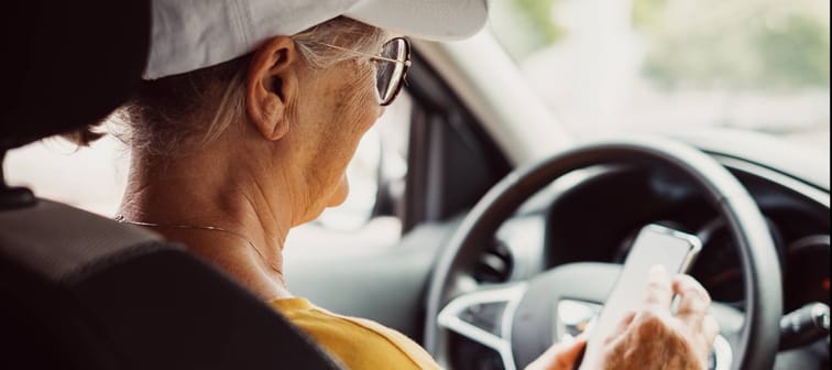 Older woman at wheel of car with phone.