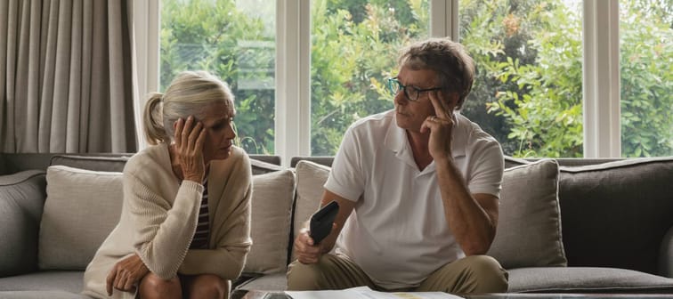 An older couple sit disturbed on a couch.