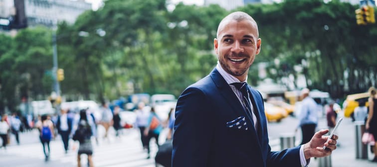 Smiling manager with smartphone looking back on street