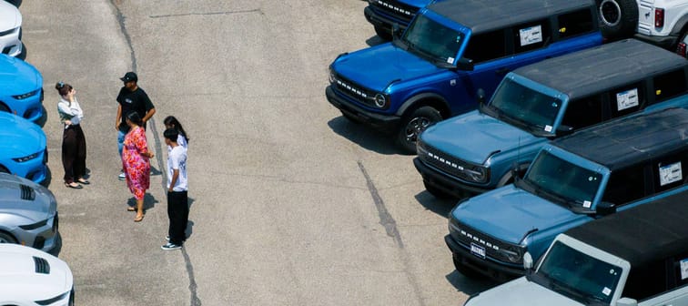 A group of people talking on a Ford car lot.