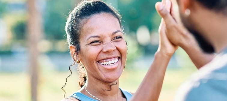A woman outdoors high-fiving someone.