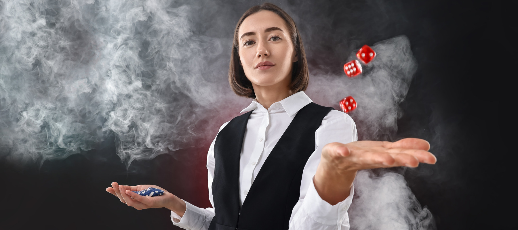 A woman in a white blouse and vest performs a magic trick as smoke drifts around her.