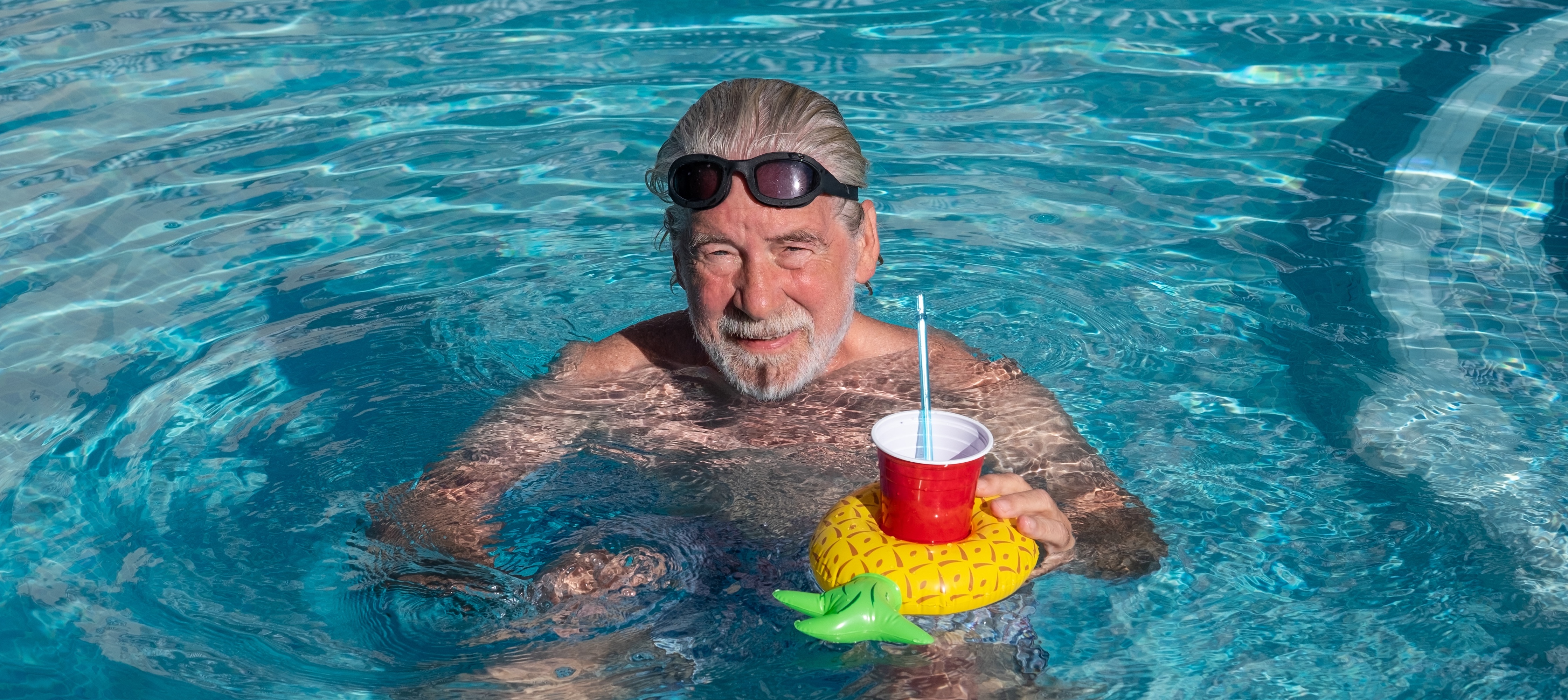 Smiling older man relaxing floating at a swimming pool in a cheerful summer vacation atmosphere.