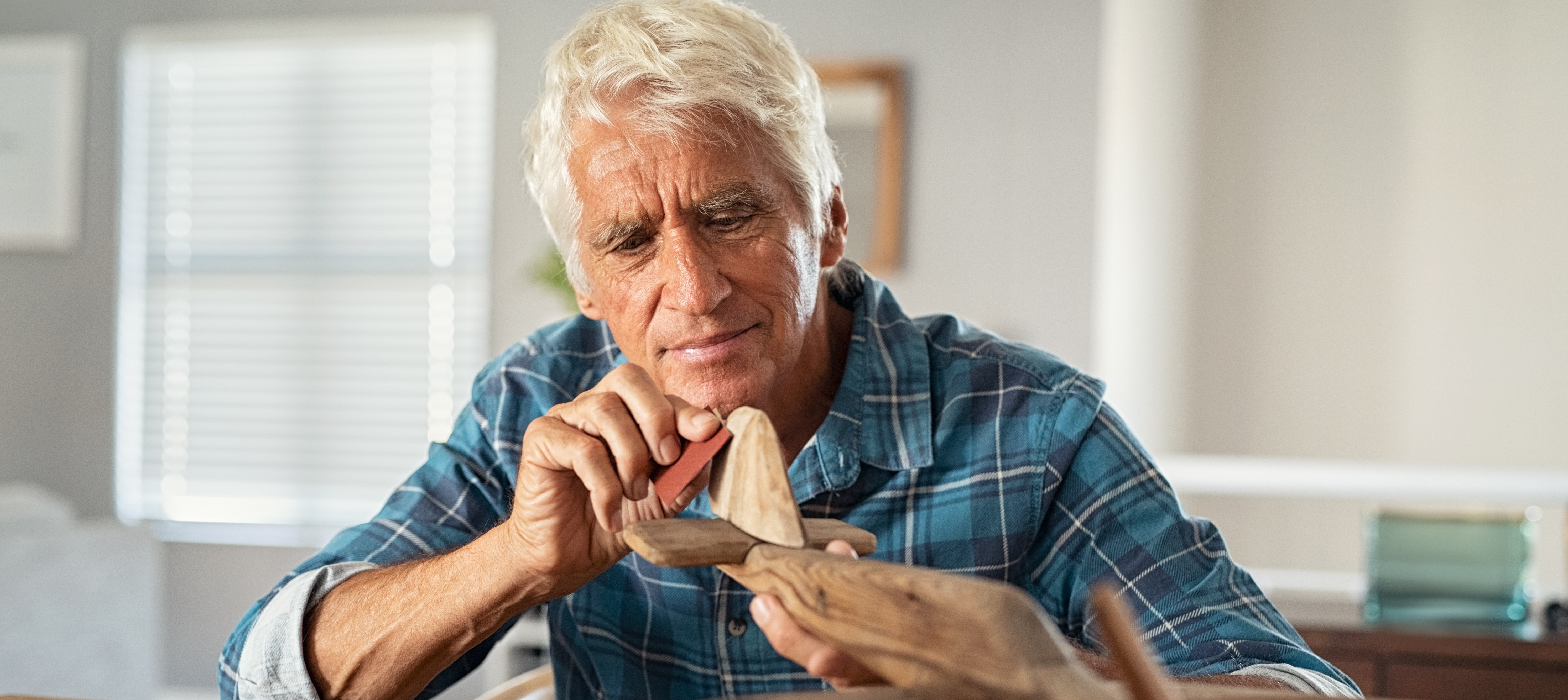 Retired man using sandpaper to polish wooden airplane sculpture.