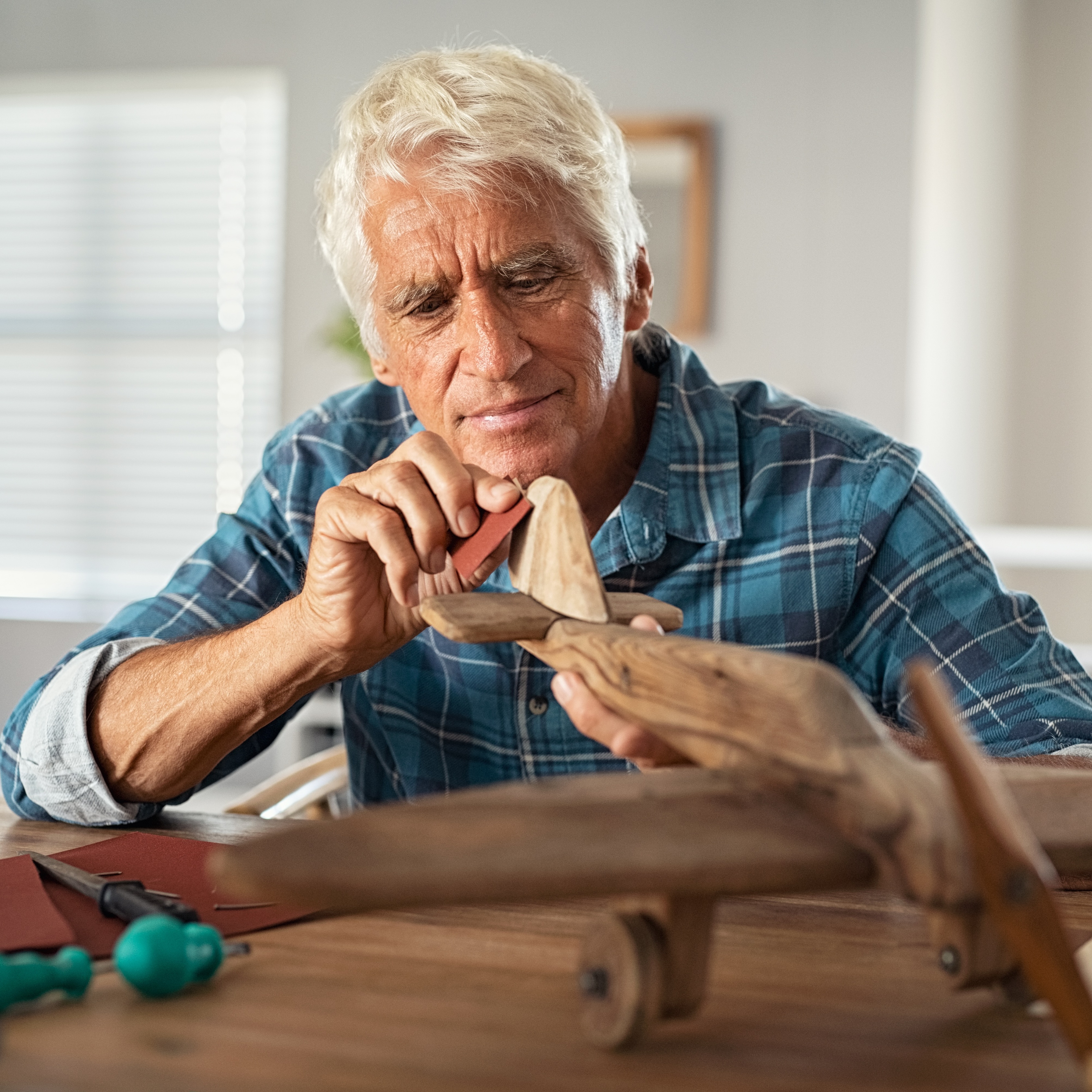 Retired man using sandpaper to polish wooden airplane sculpture.
