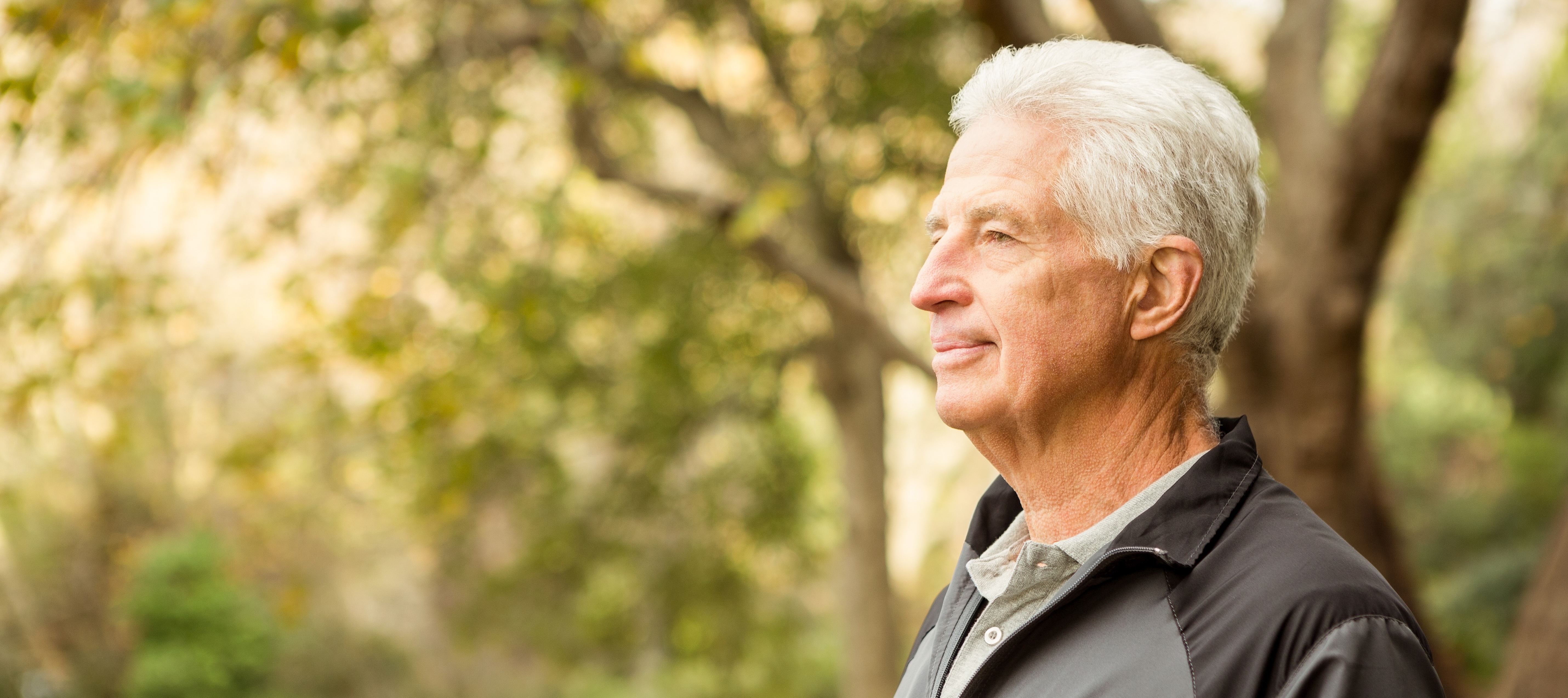 Top half of an older man in a park looking off to the side.