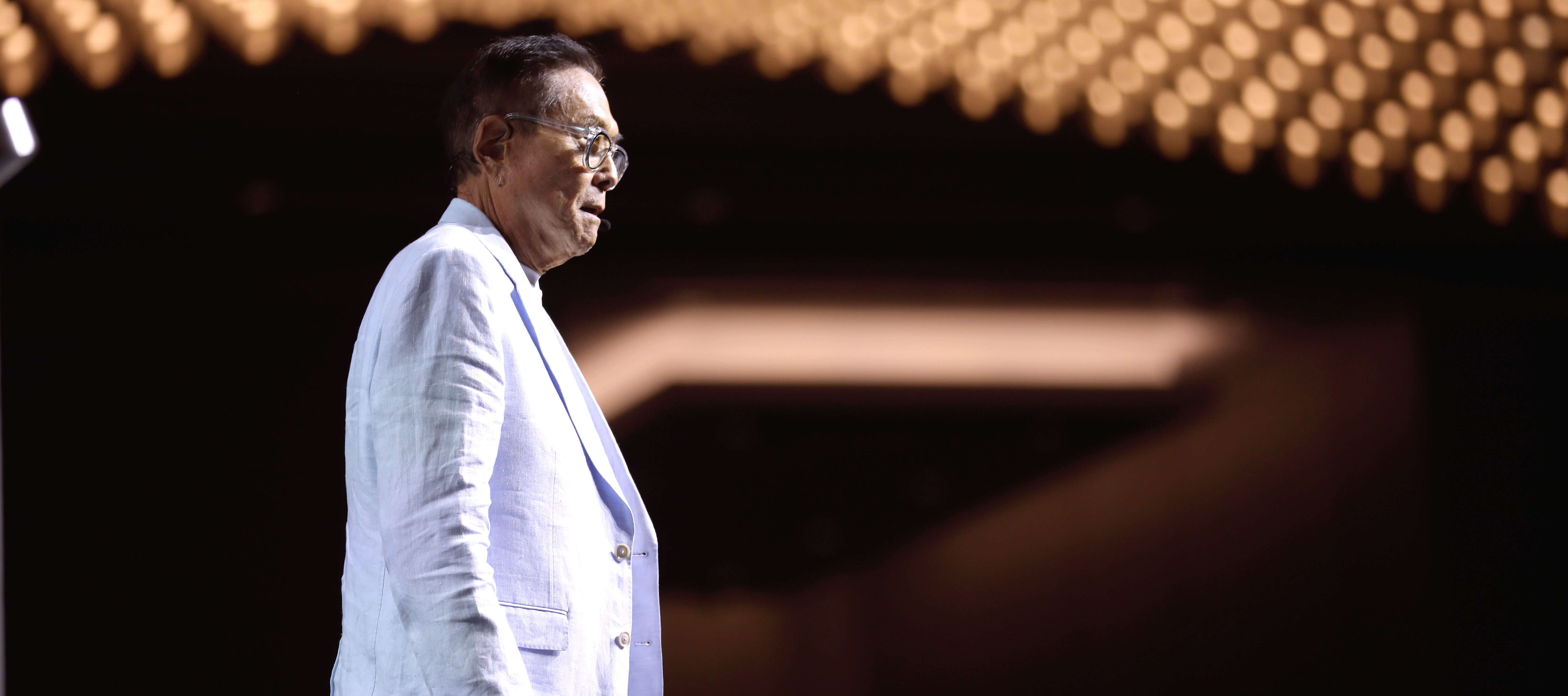 Robert Kiyosaki stands on stage with banks of lights in the background
