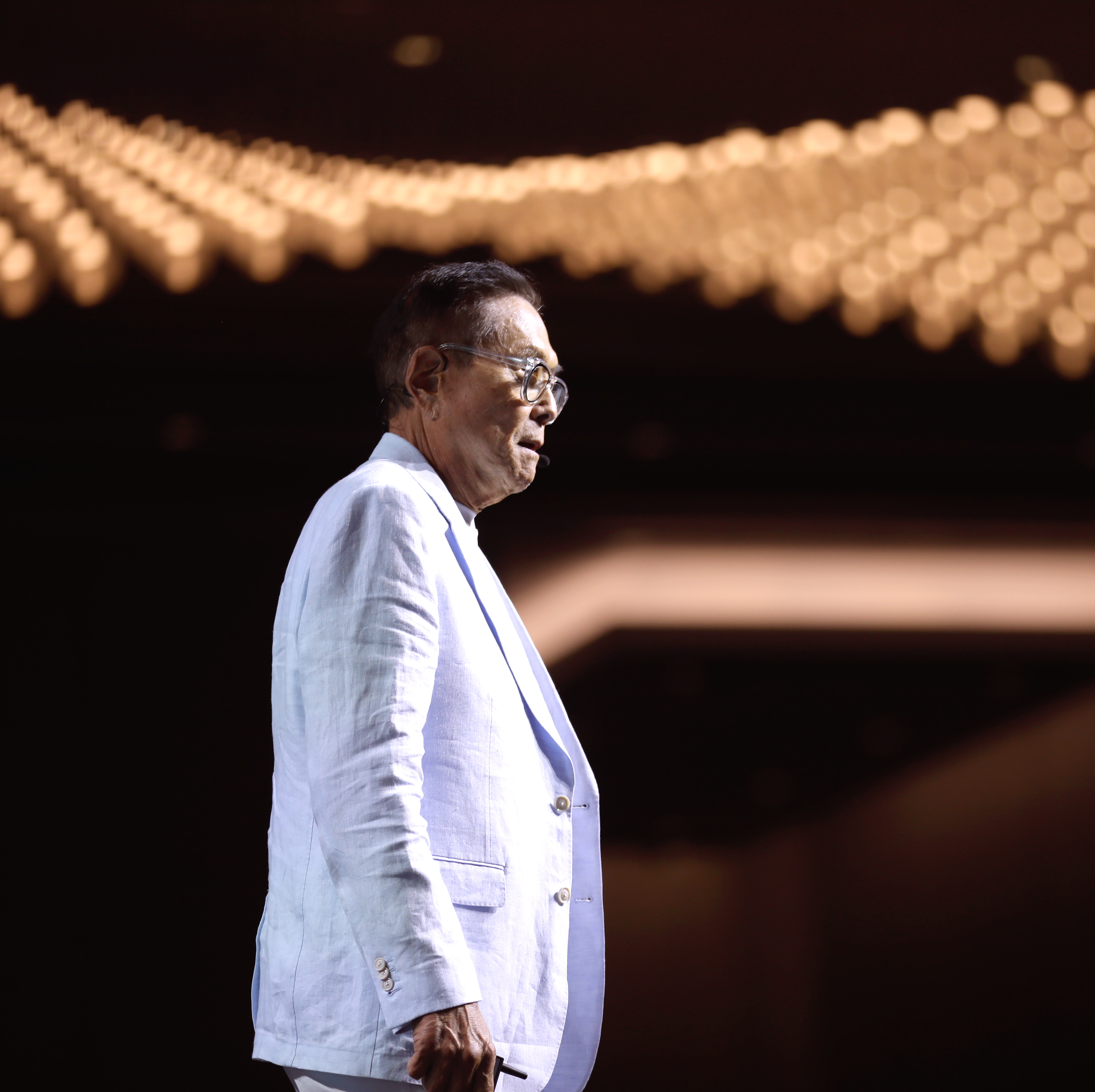 Robert Kiyosaki stands on stage with banks of lights in the background