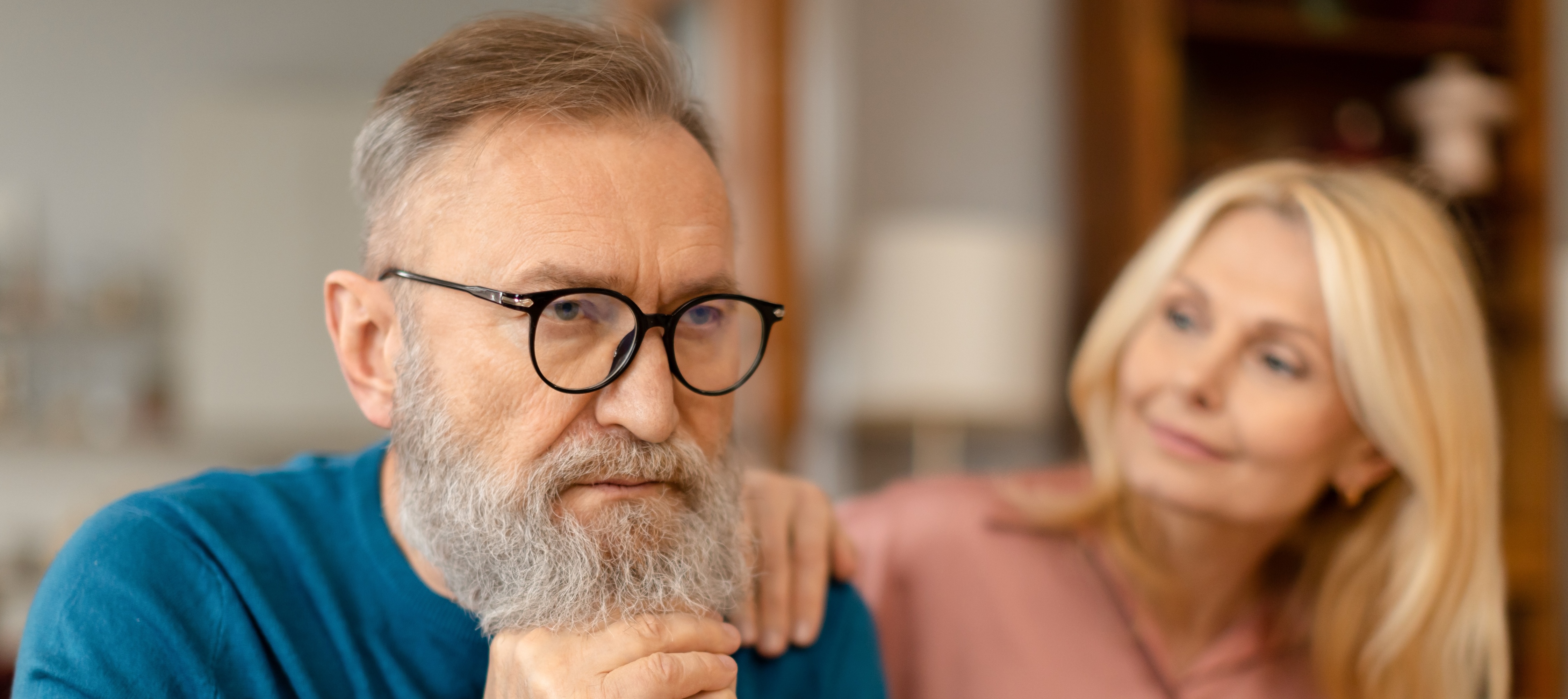 Attentive senior lady comforting her concerned husband, touching his shoulder.