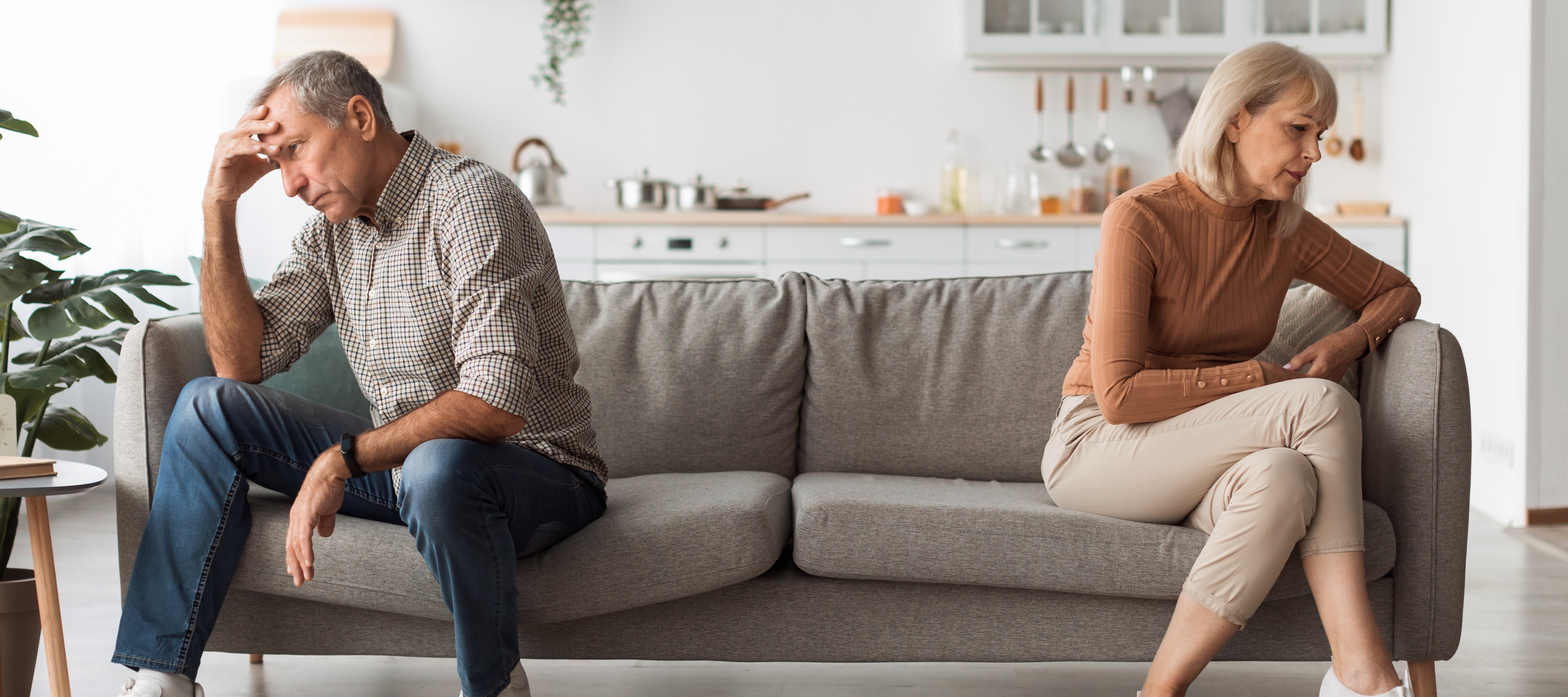 Unhappy older couple sitting back-to-back on a couch.
