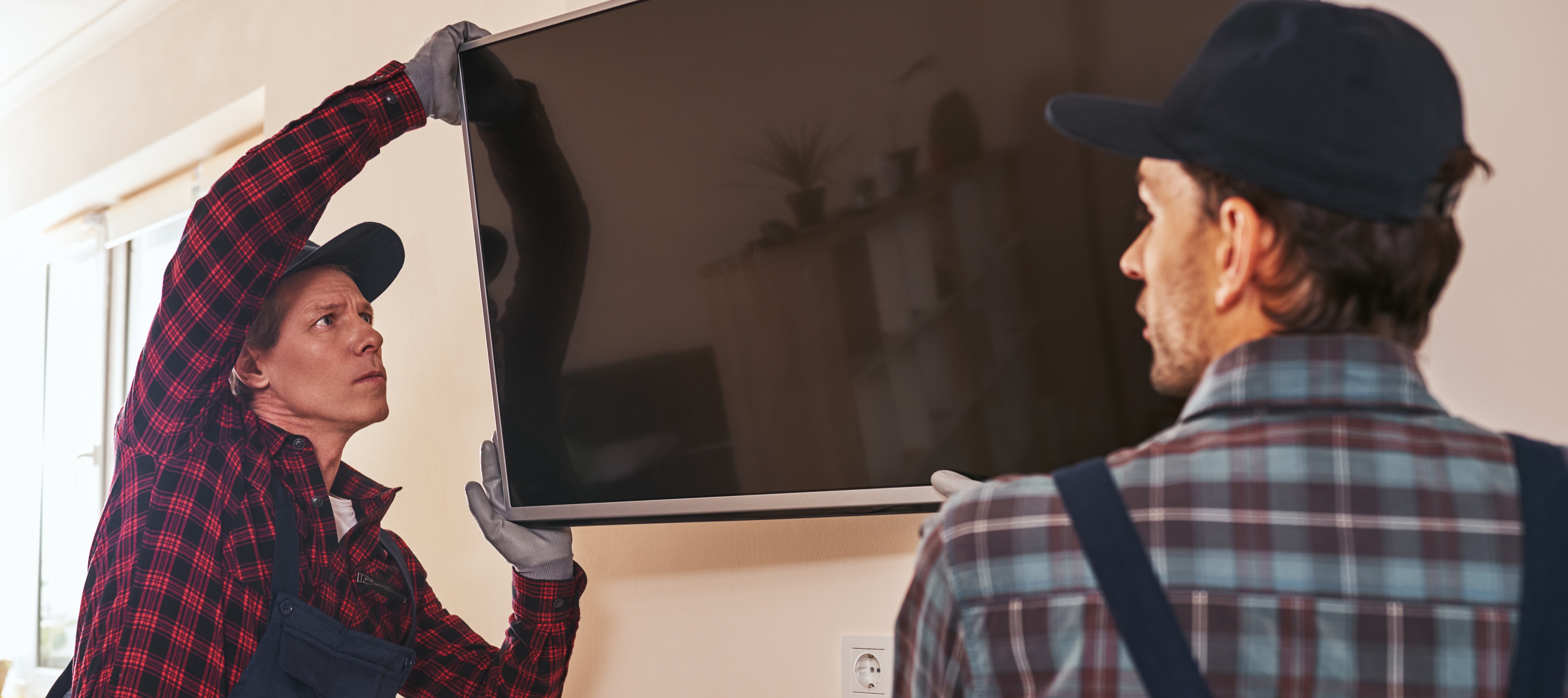 Two men hang a large TV on a wall mount.