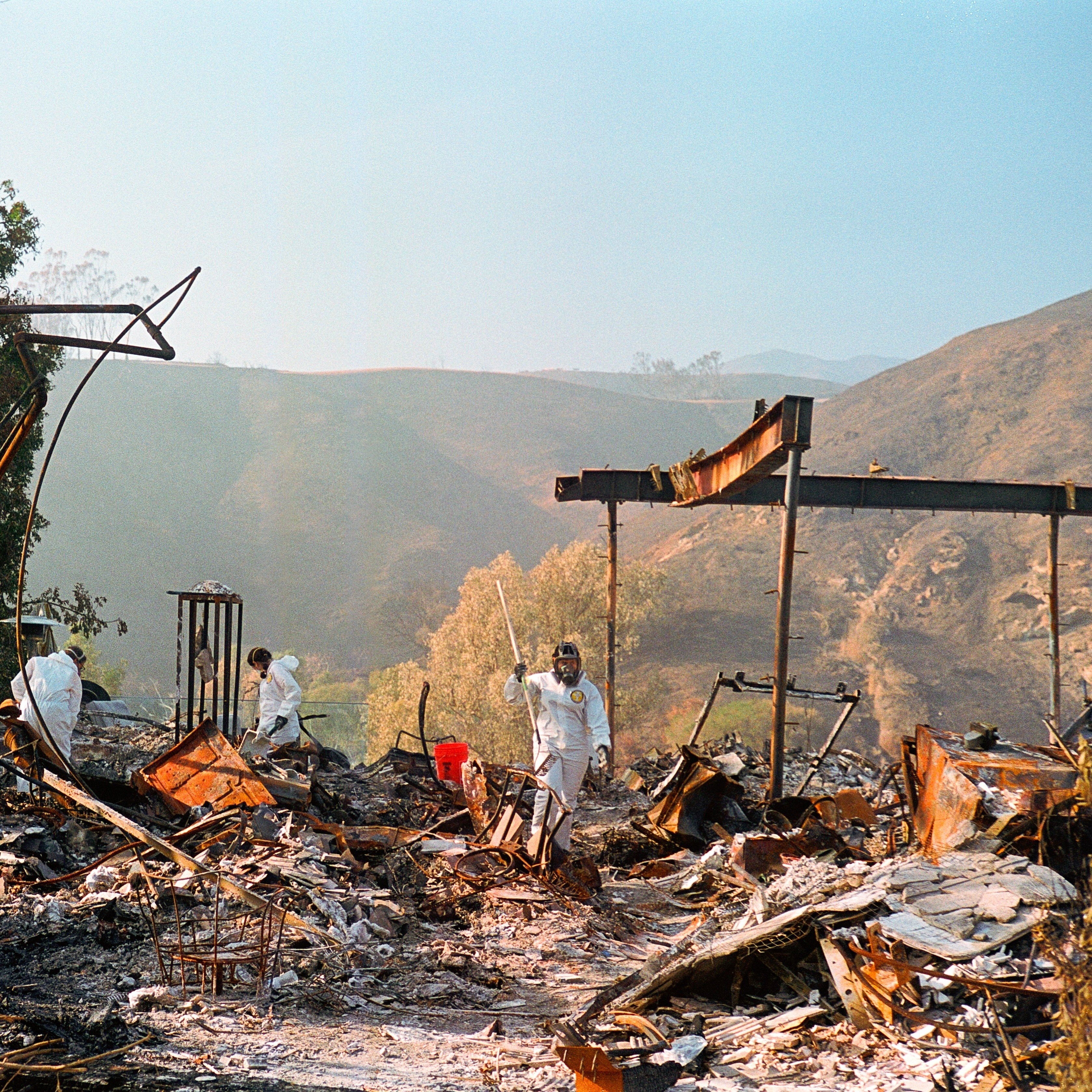 People in protective suits dig through the rubble of a home destroyed in the LA wildfires in 2025.