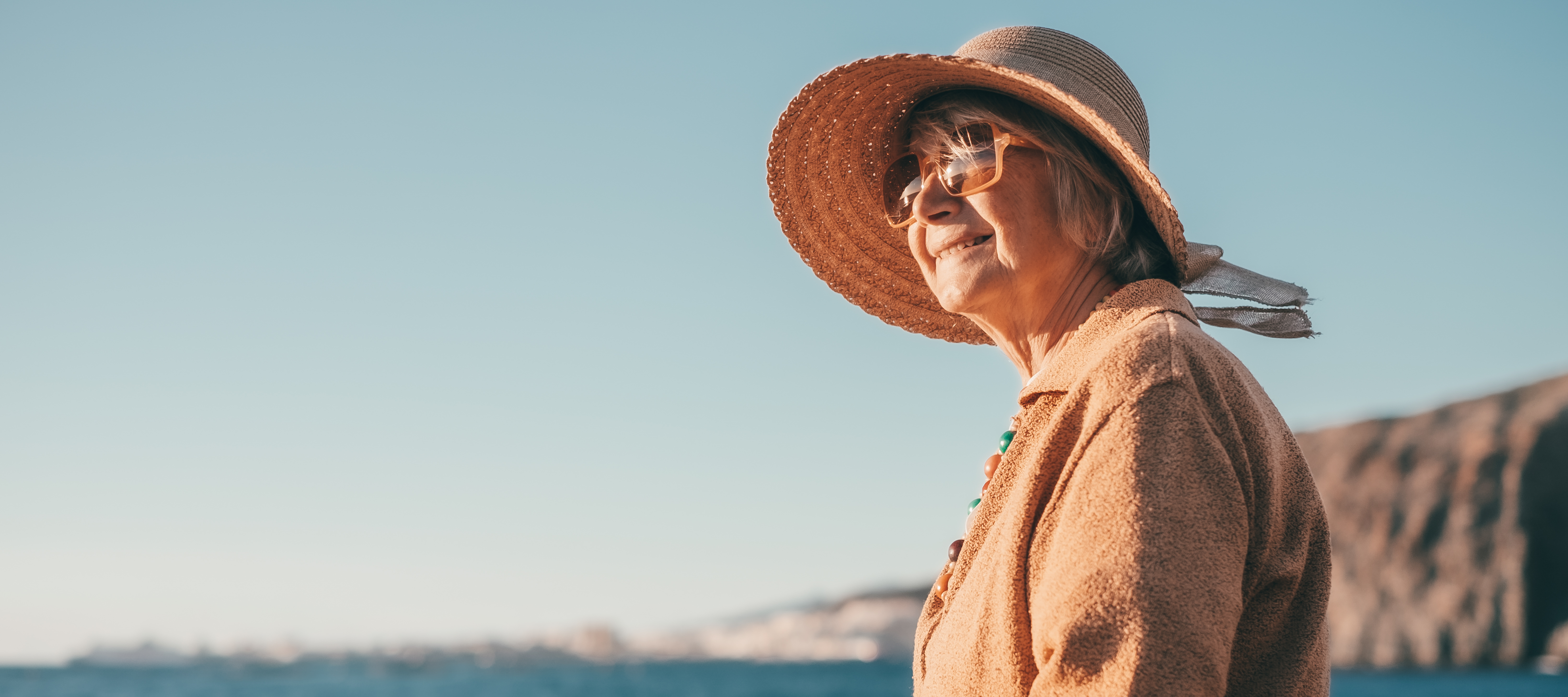 Smiling senior woman sitting, facing the sea reading a book.