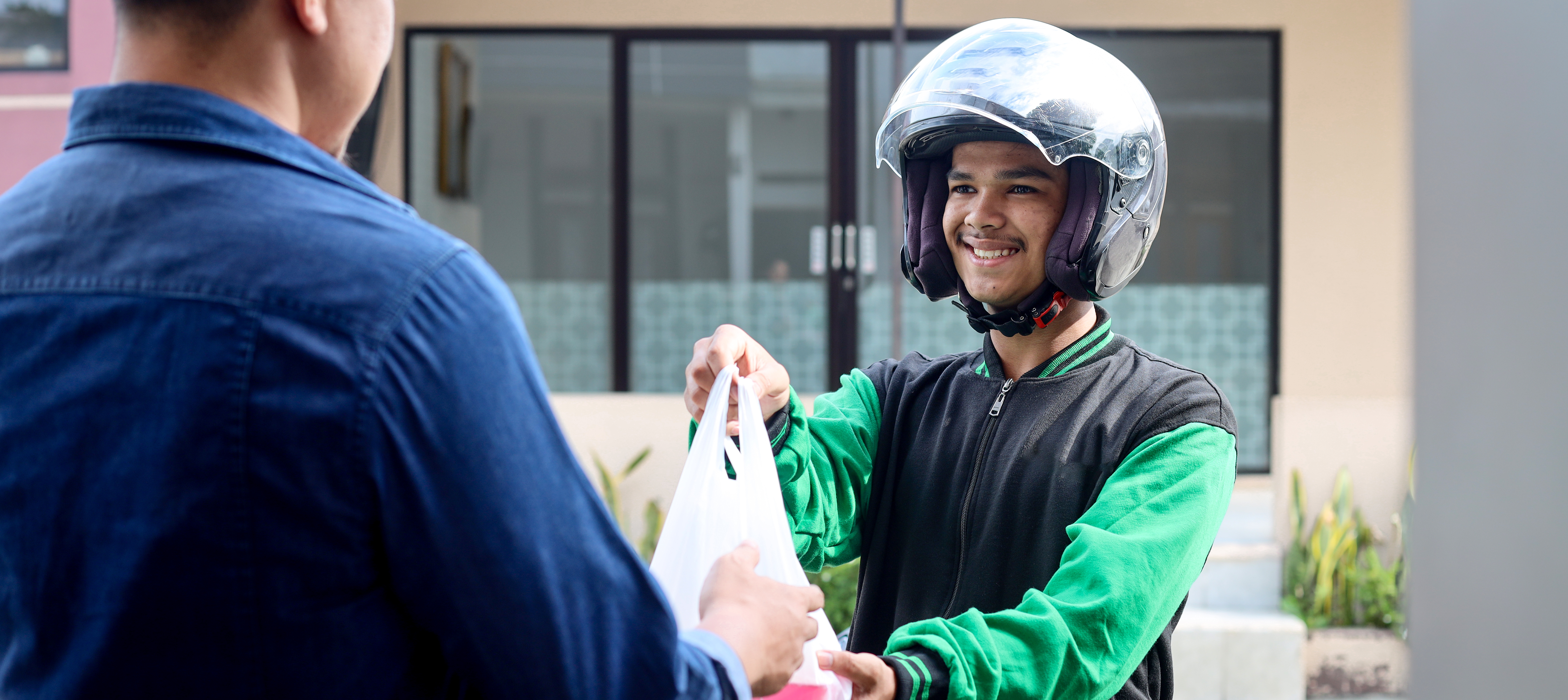 Food deliveryman on a bike with a helmet handing package to customer.