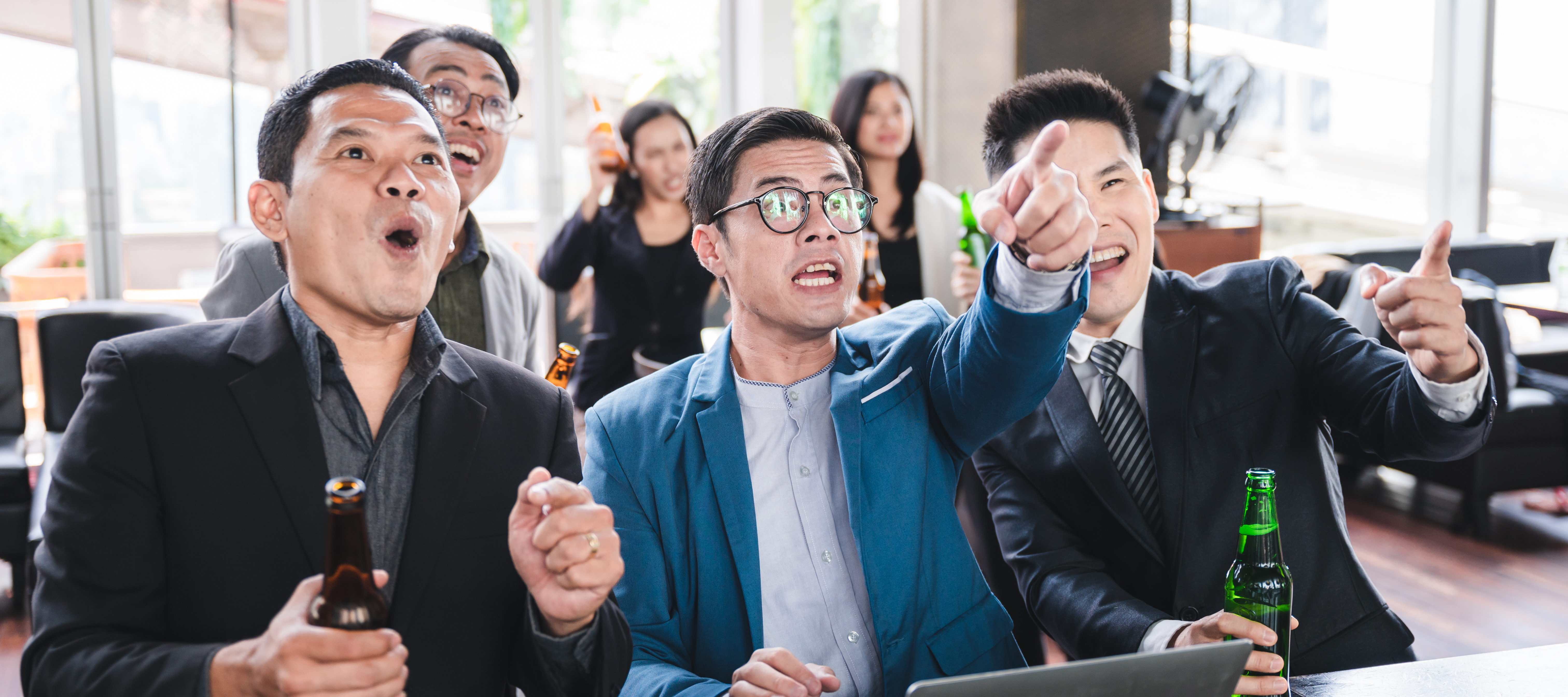 Group of businessmen in an office setting yelling excitedly and pointing.
