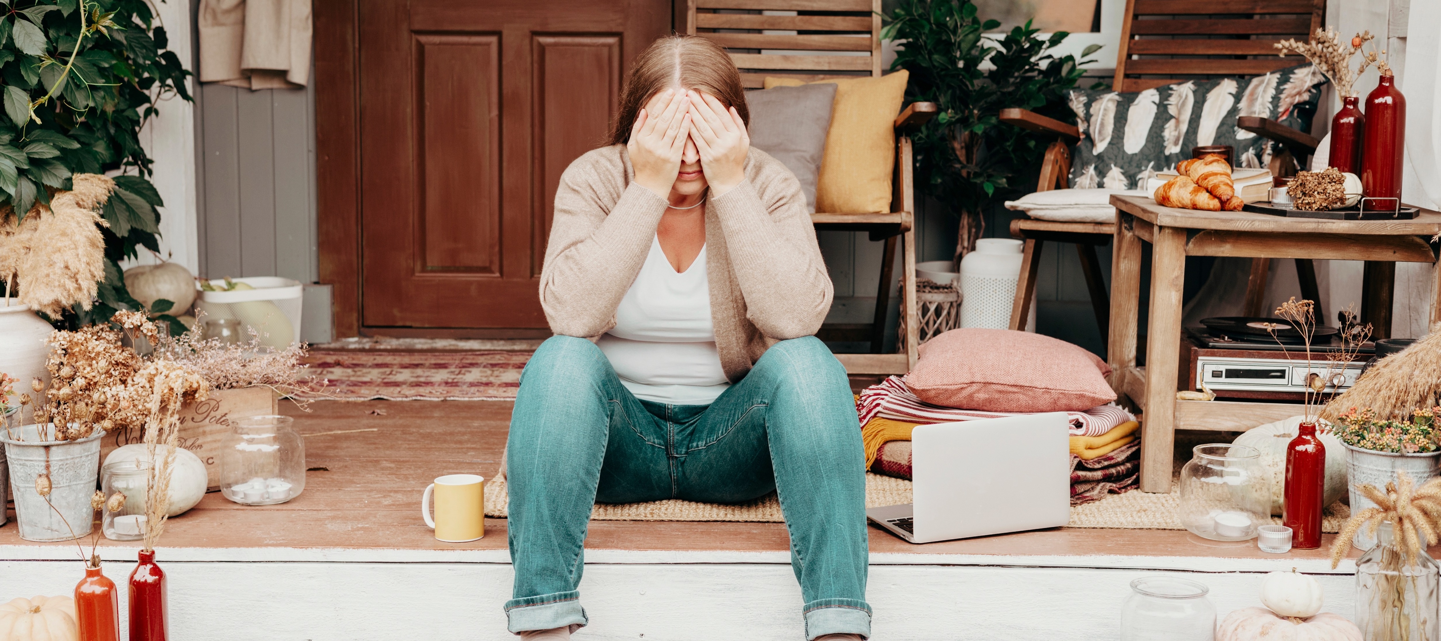 Woman sits on the front porch of her home with her hands over her face, looking stressed.