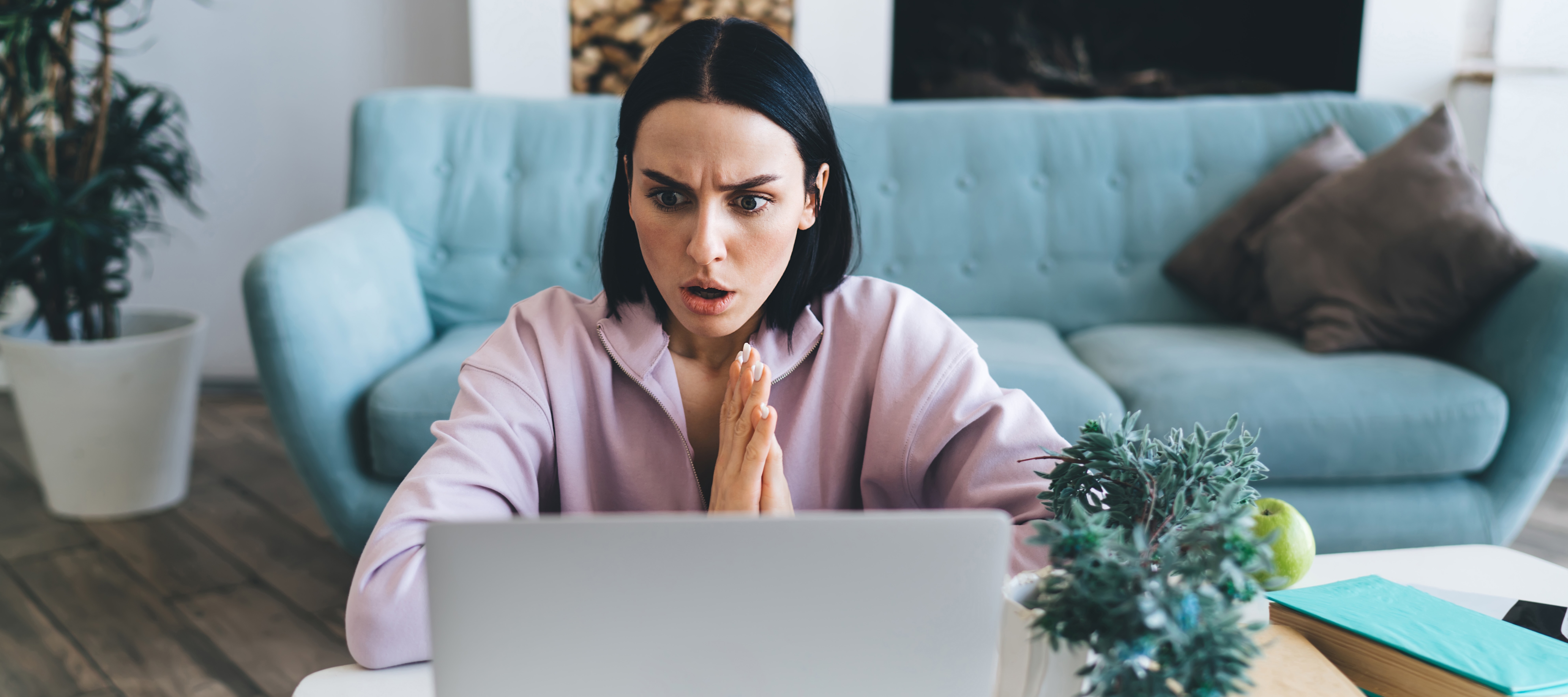 Woman sitting at coffee table with shocked expression on her face while on a video call on her laptop.