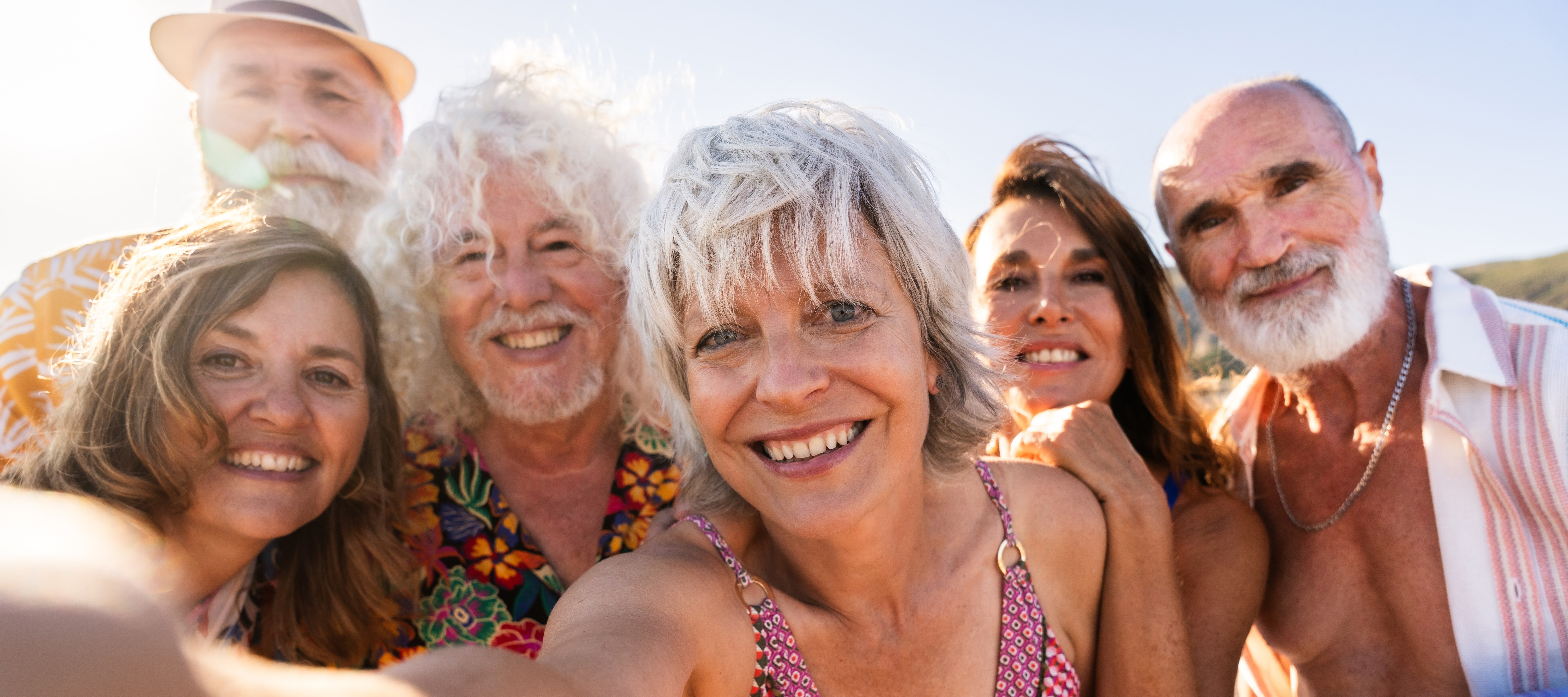 Selfie of retired adults of various ages, smiling on a beach.