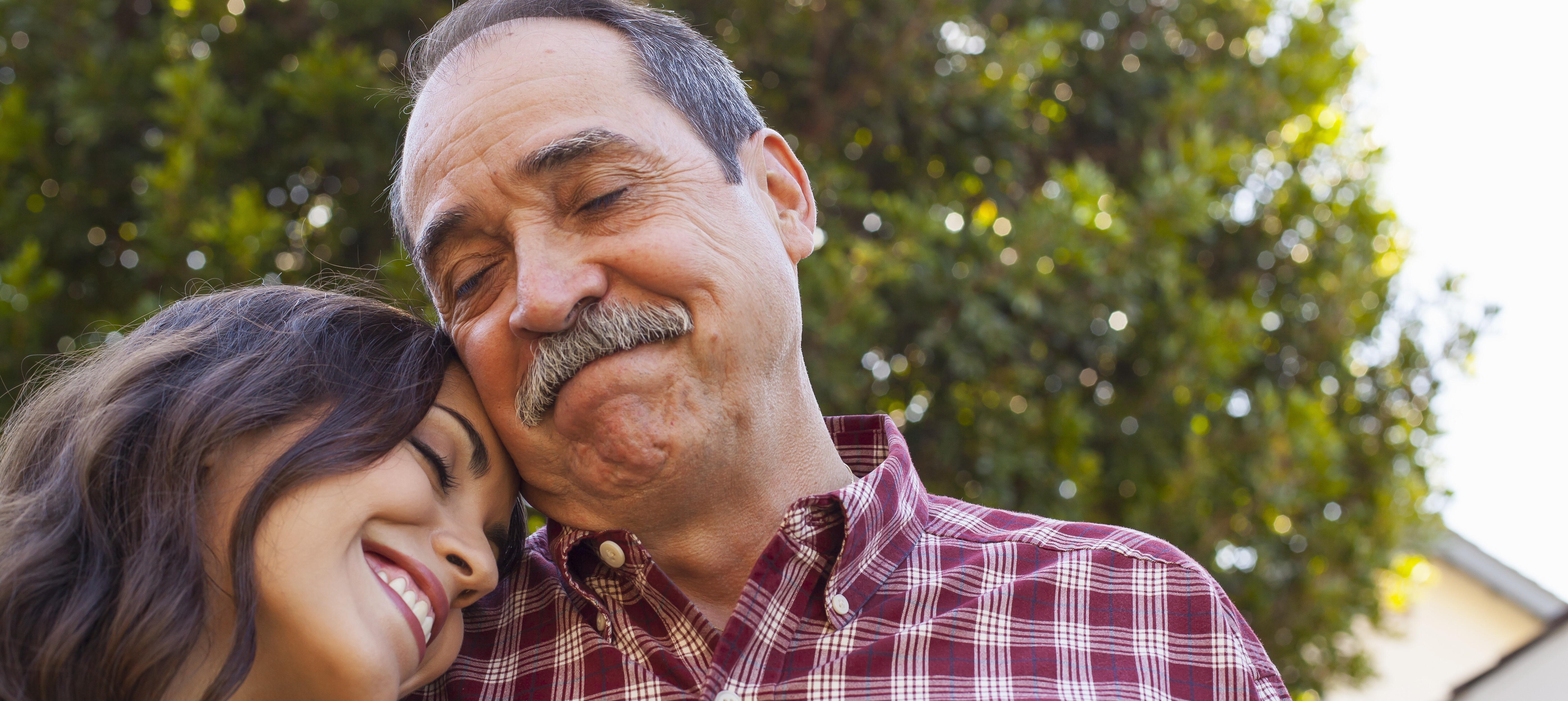 Adult daughter resting her head on father's shoulder while they both smile.